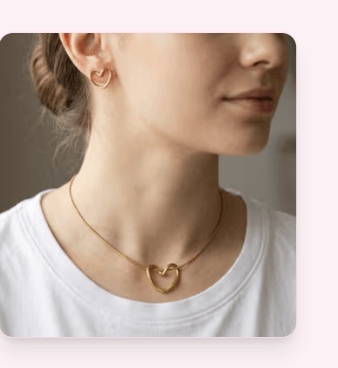 Model in a white tee wearing matte gold open-heart stud earrings and a matching heart pendant necklace.